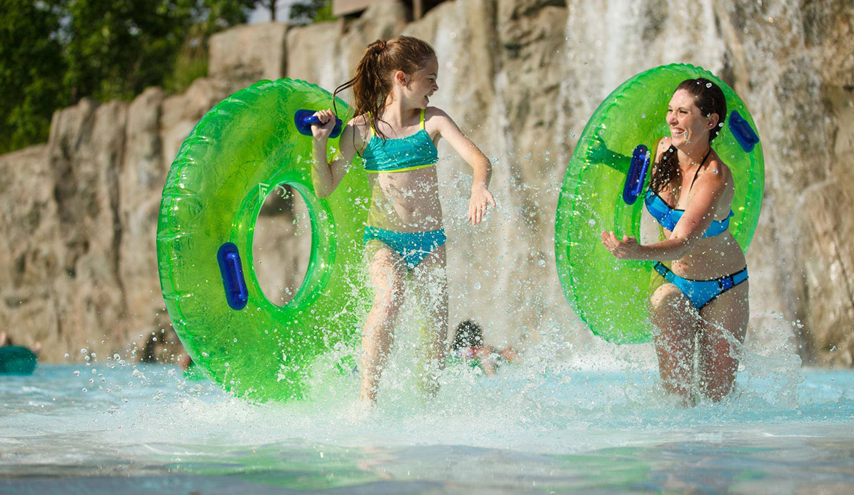 A woman and girl run with innertubes at a swim park photo shoot.