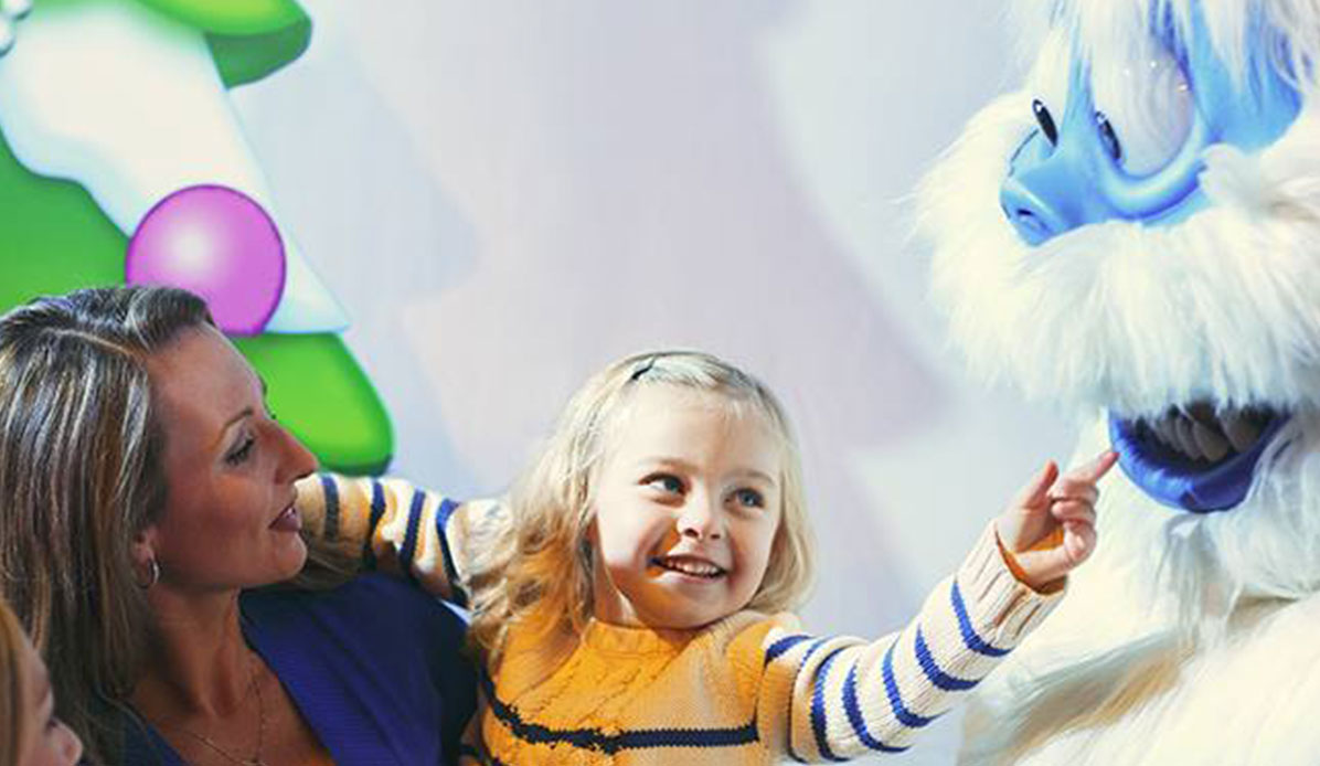 A woman and girl smile at a theme park mascot.
